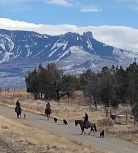 people riding horses with mountains and clouds